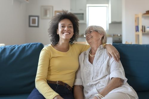 An elderly mother poses with her adopted African American daughter as they sit on the sofa in the living room concept